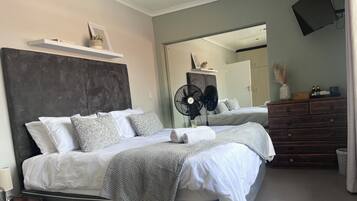 A modern bedroom with a large bed, bedside tables, a dresser, and a wall-mounted fan.