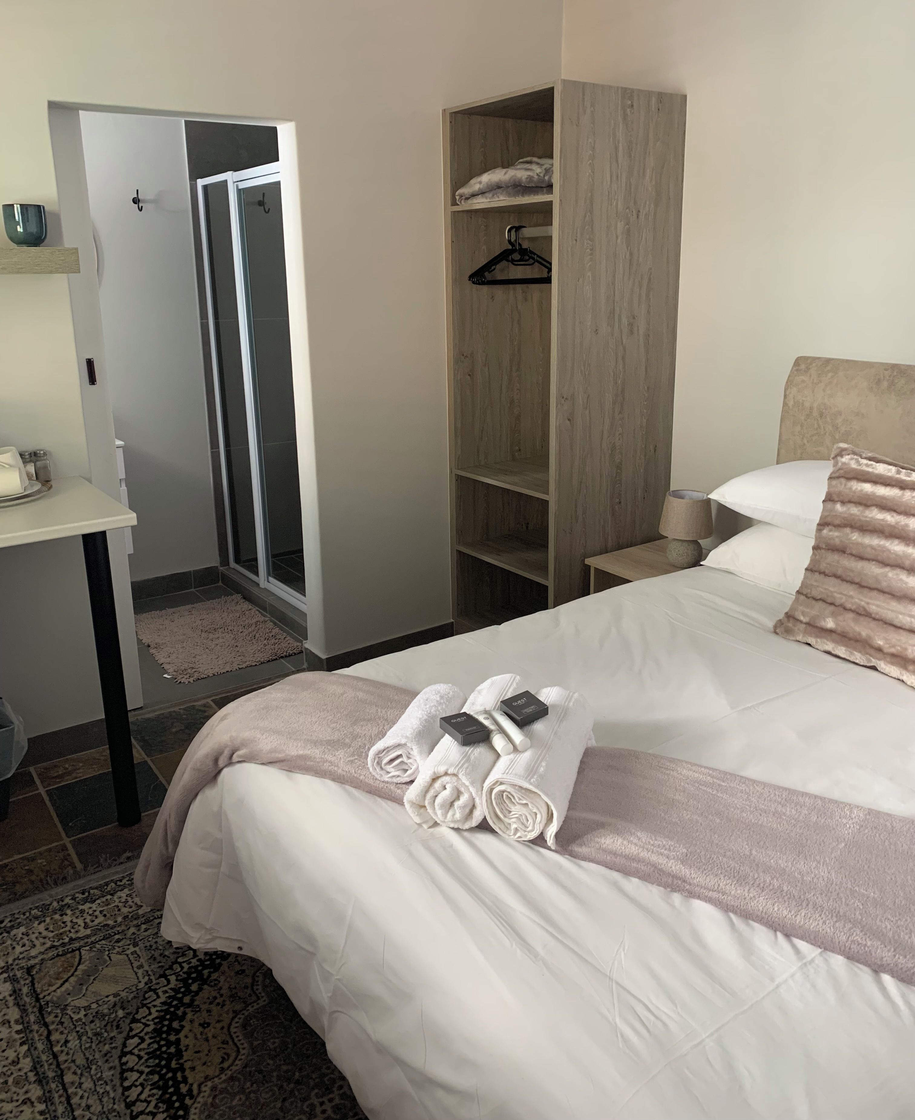 A hotel room with a bed, a bedside table, a wardrobe, and a bathroom with a shower.