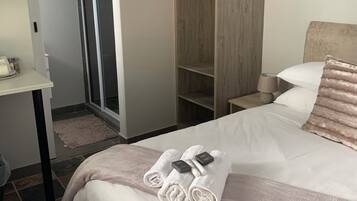 A hotel room with a bed, a bedside table, a wardrobe, and a bathroom with a shower.