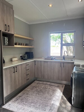 A modern kitchen with wooden cabinets, a built-in stove, a sink, and a window providing natural light. - Santorini Guesthouse (East London)