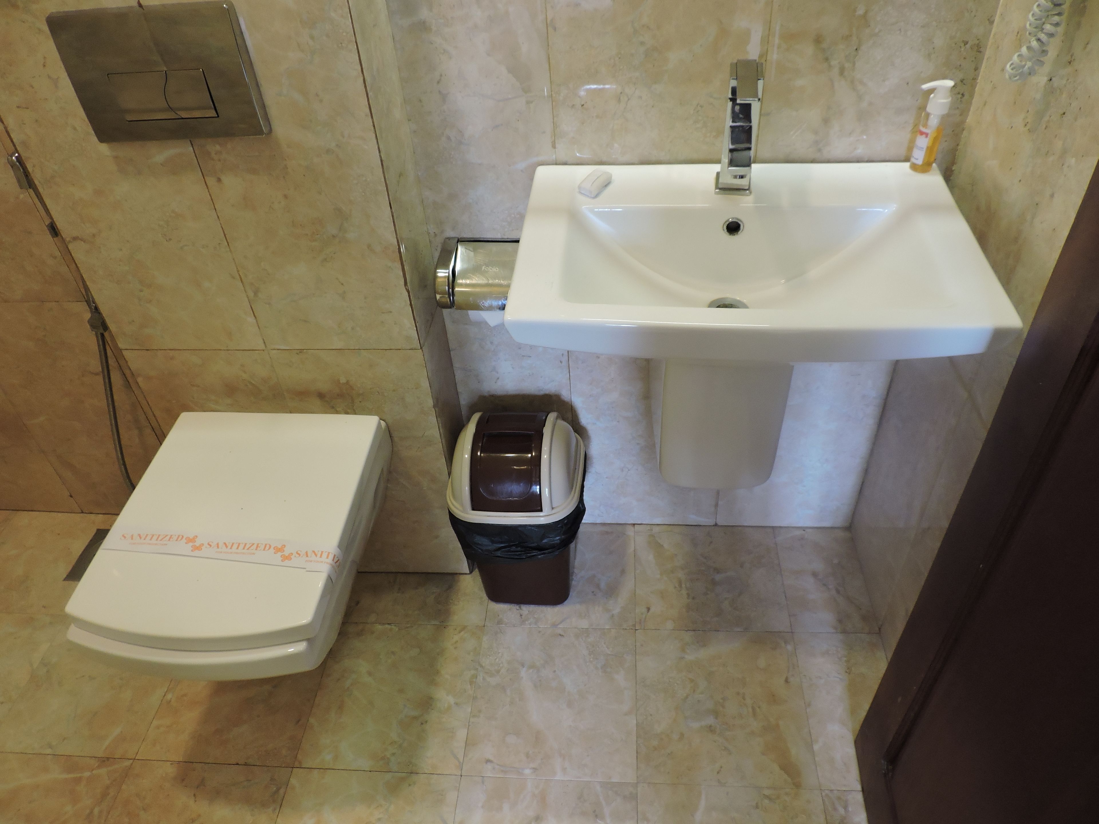 A bathroom with a toilet, a sink, and a trash bin.