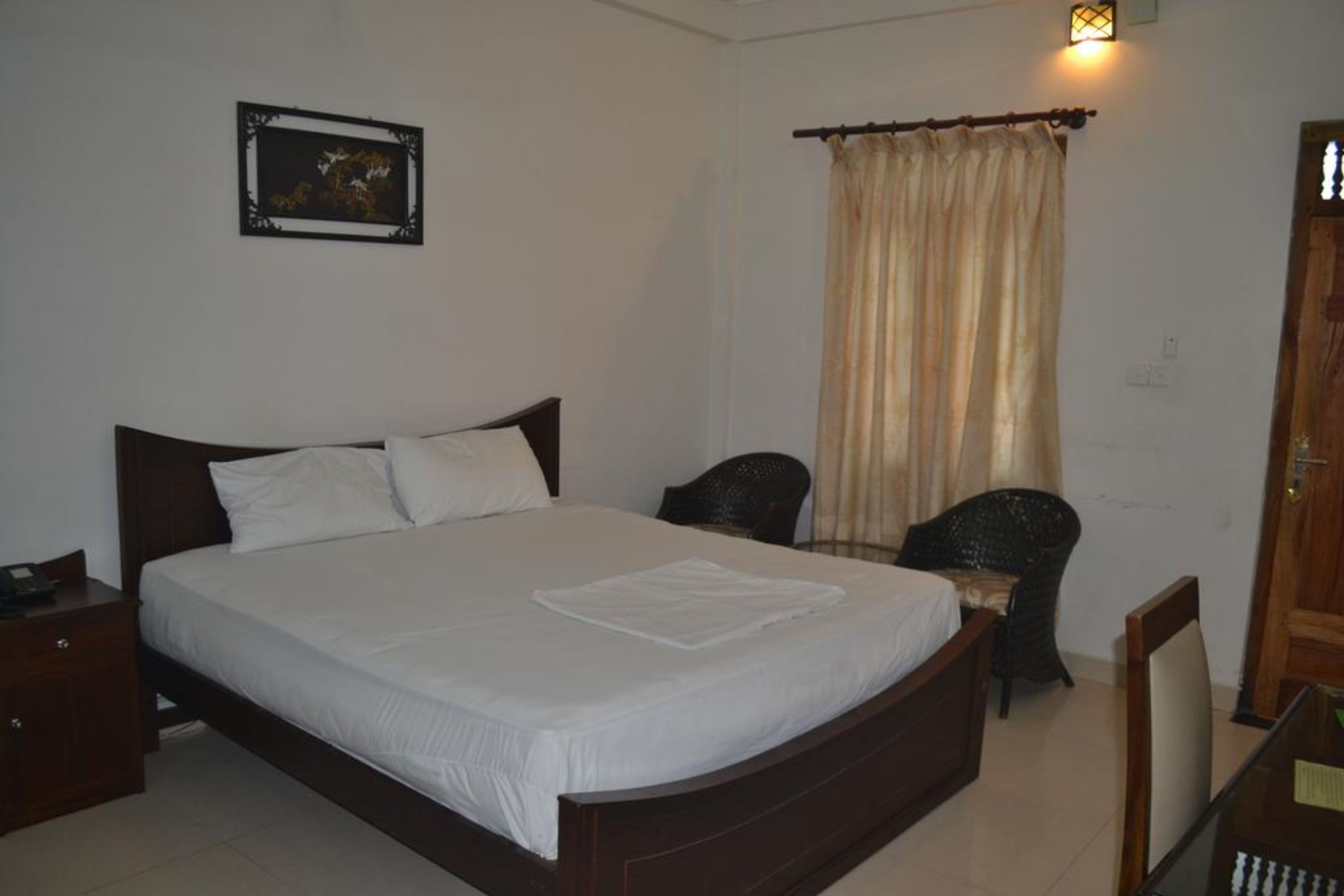 A bedroom with a large bed, a nightstand, a chair, a desk, and a window with curtains.
