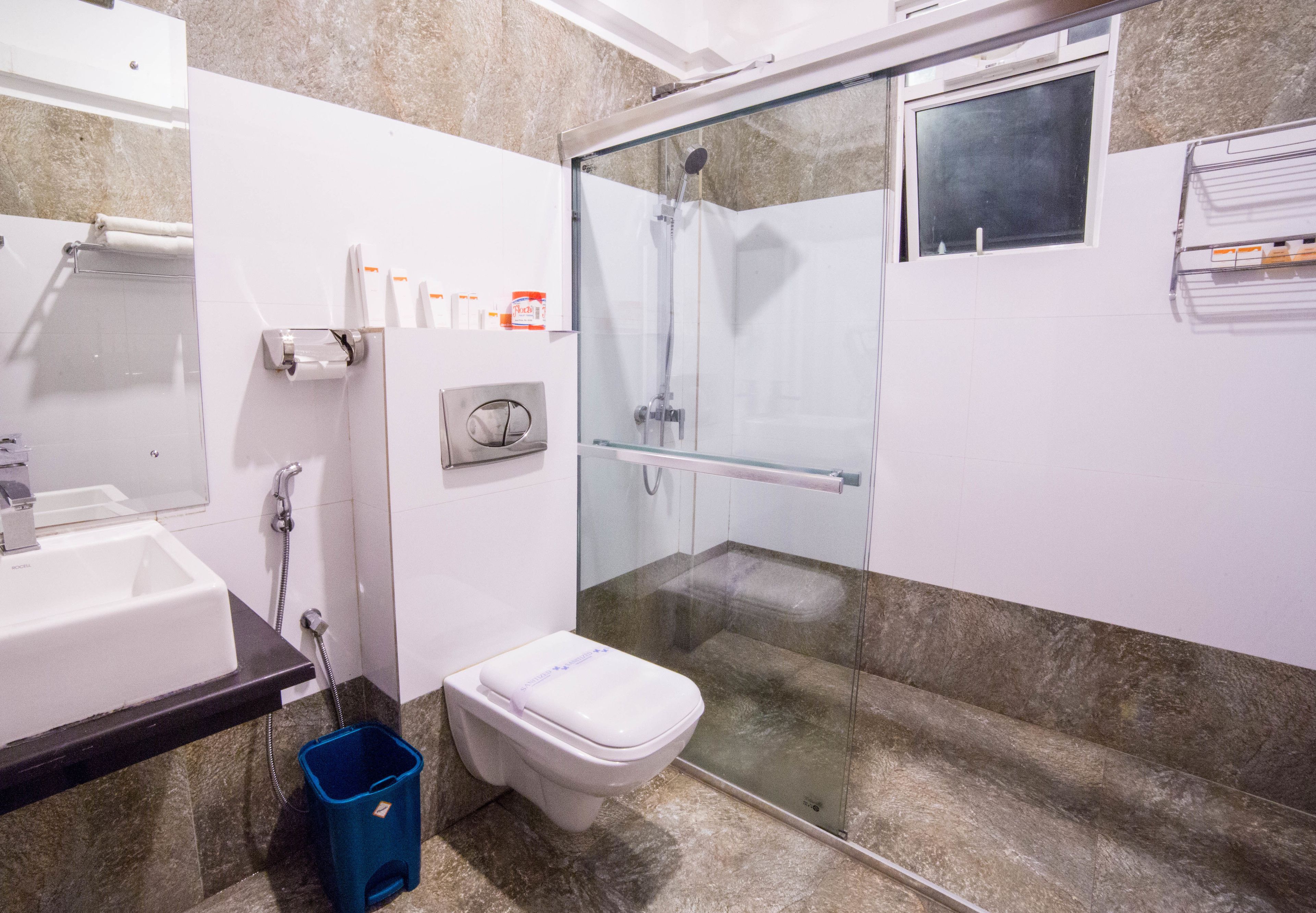 A modern bathroom with a glass-enclosed shower, a white toilet, a sink, and a blue trash bin.