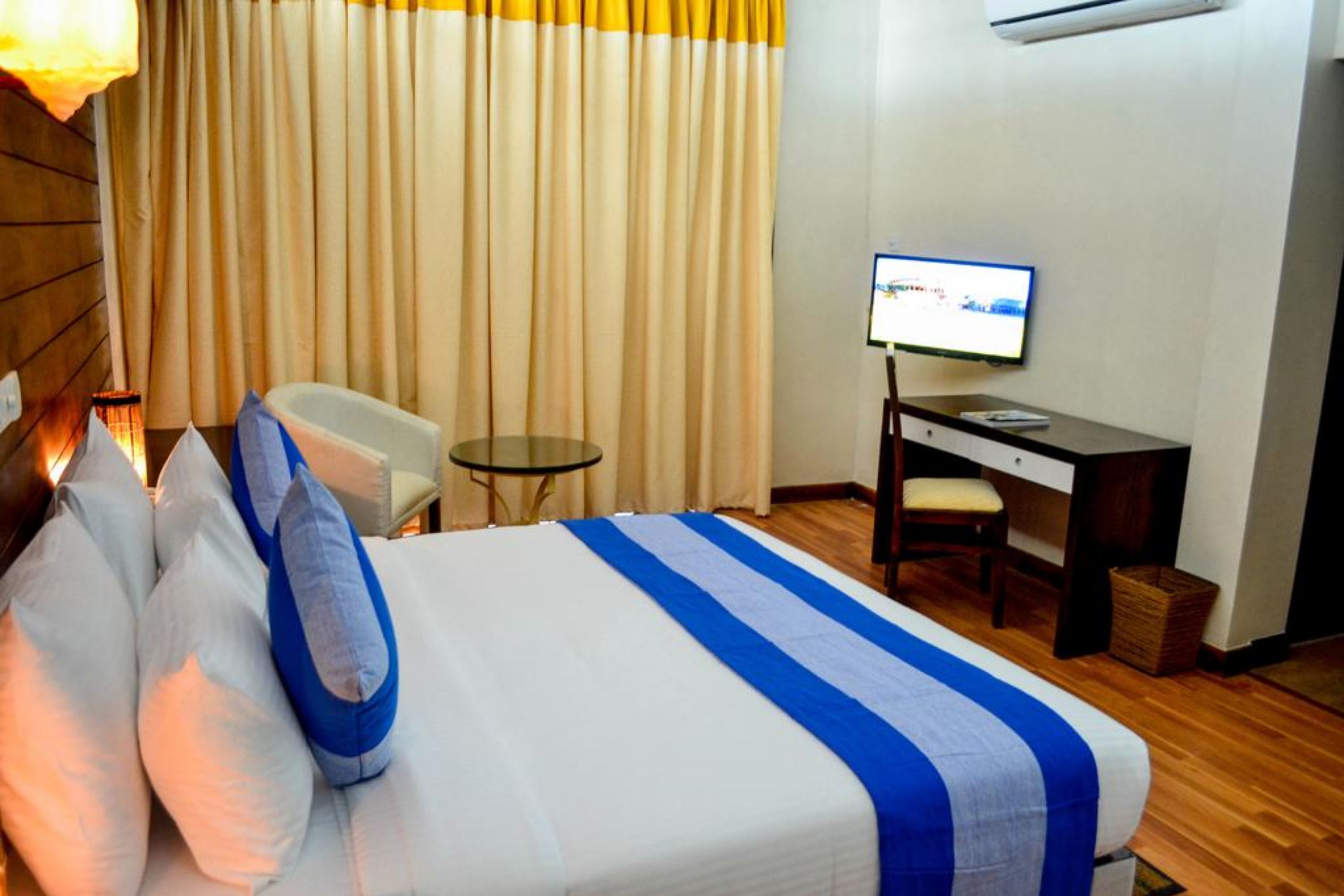 A hotel room with a bed, a desk, a chair, a small table, and a television.