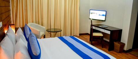 A hotel room with a bed, a desk, a chair, a small table, and a television.