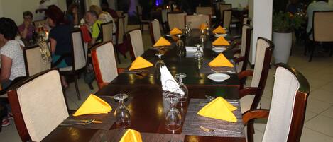 Un restaurante con varias mesas dispuestas, con servilletas amarillas, cubiertos y copas de vino.