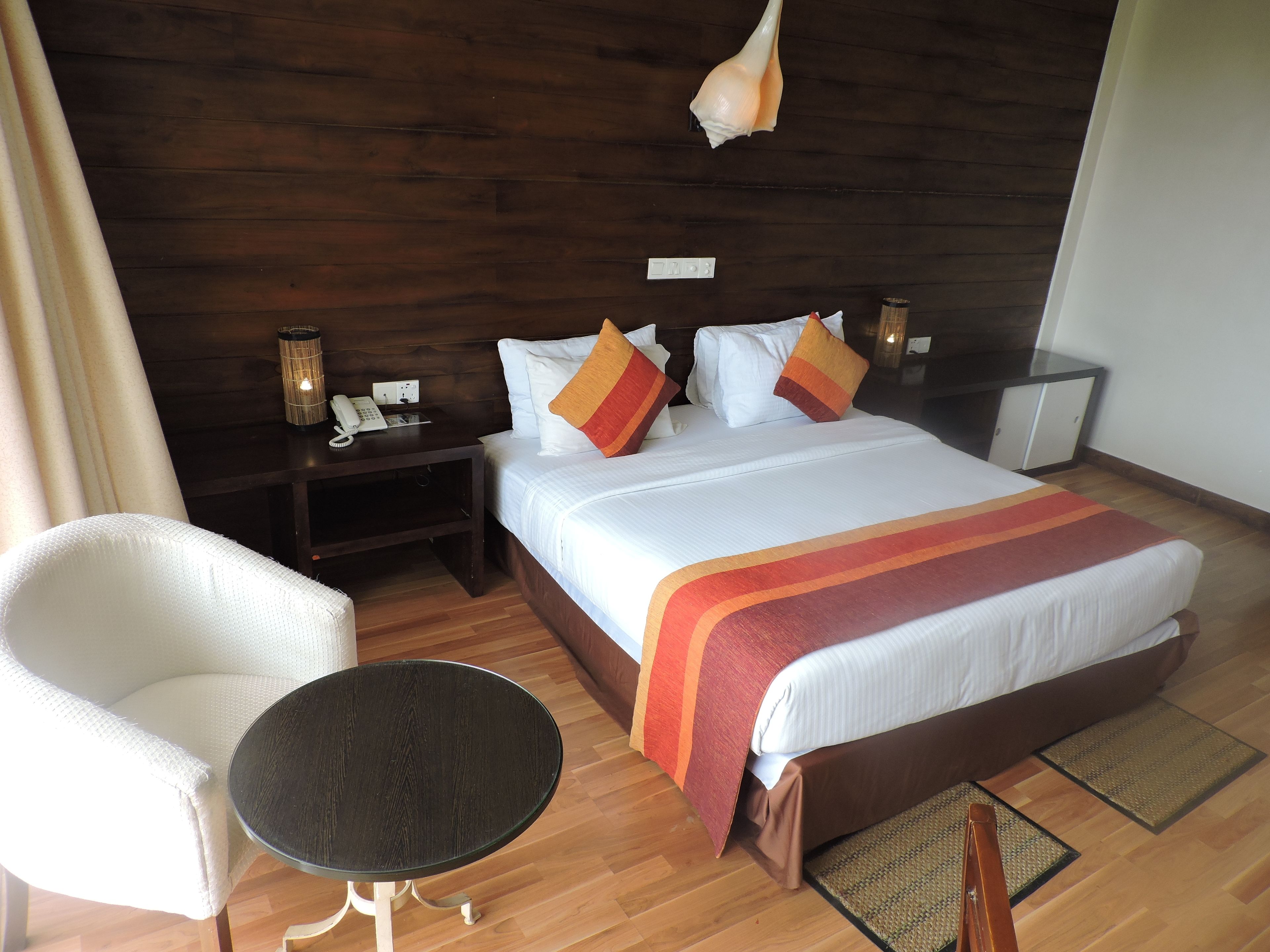 A hotel room with a large bed, a bedside table with a lamp, a chair, and a small round table.