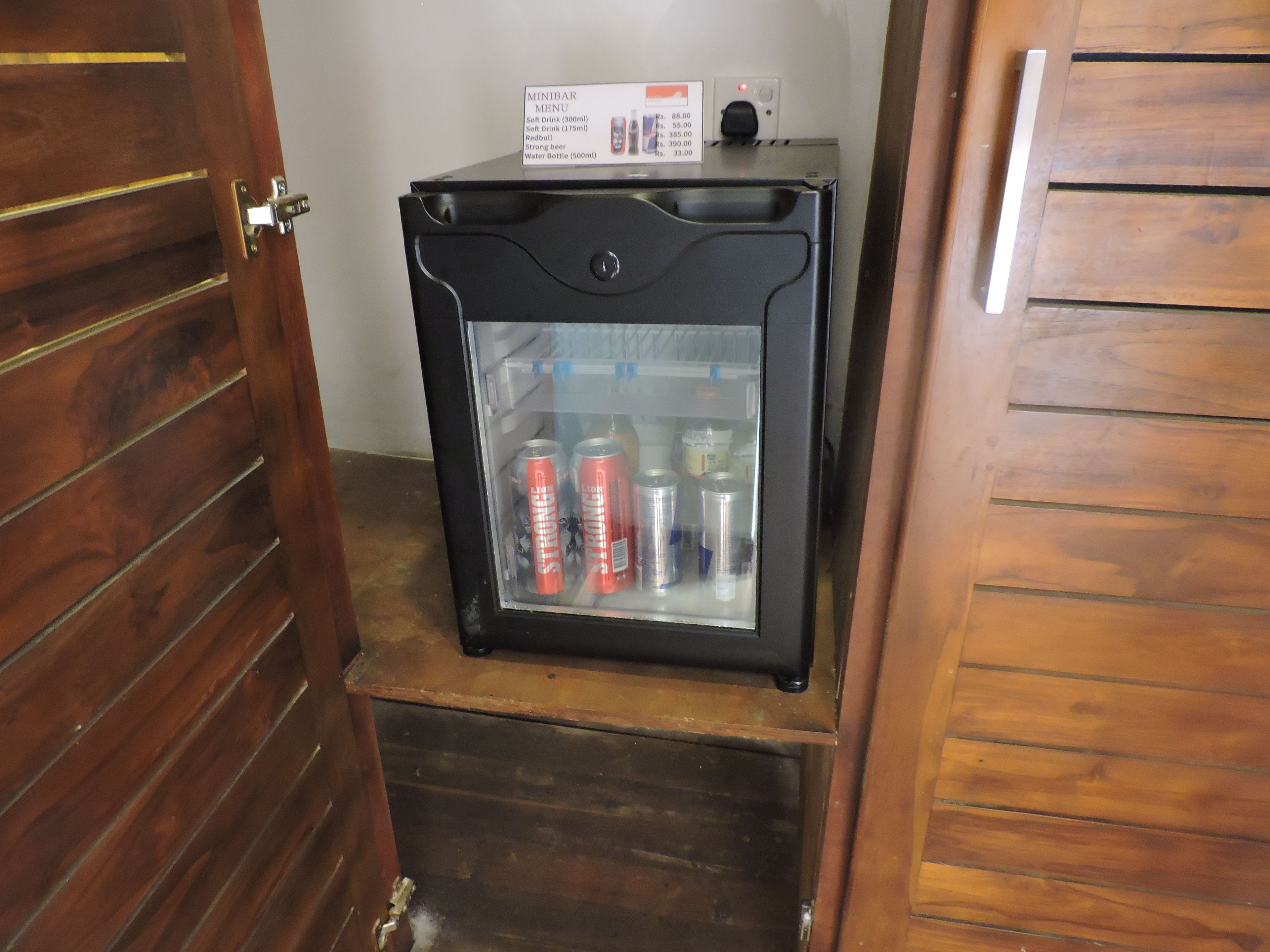 A minibar with a glass door, containing cans of beverages and a water bottle.