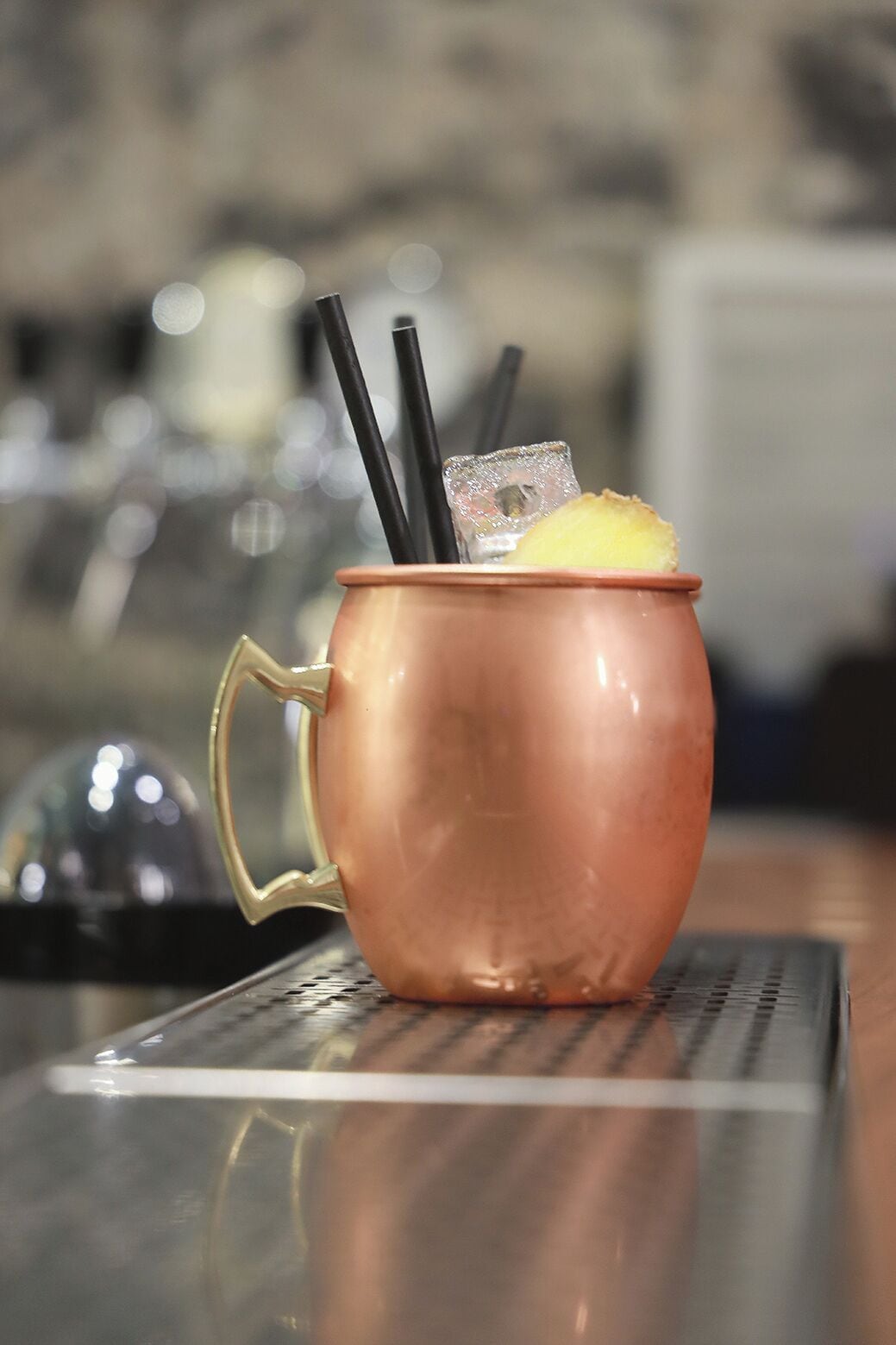 Un vaso de cobre con una rodaja de limón y pajitas negras sobre un tapete de bar.