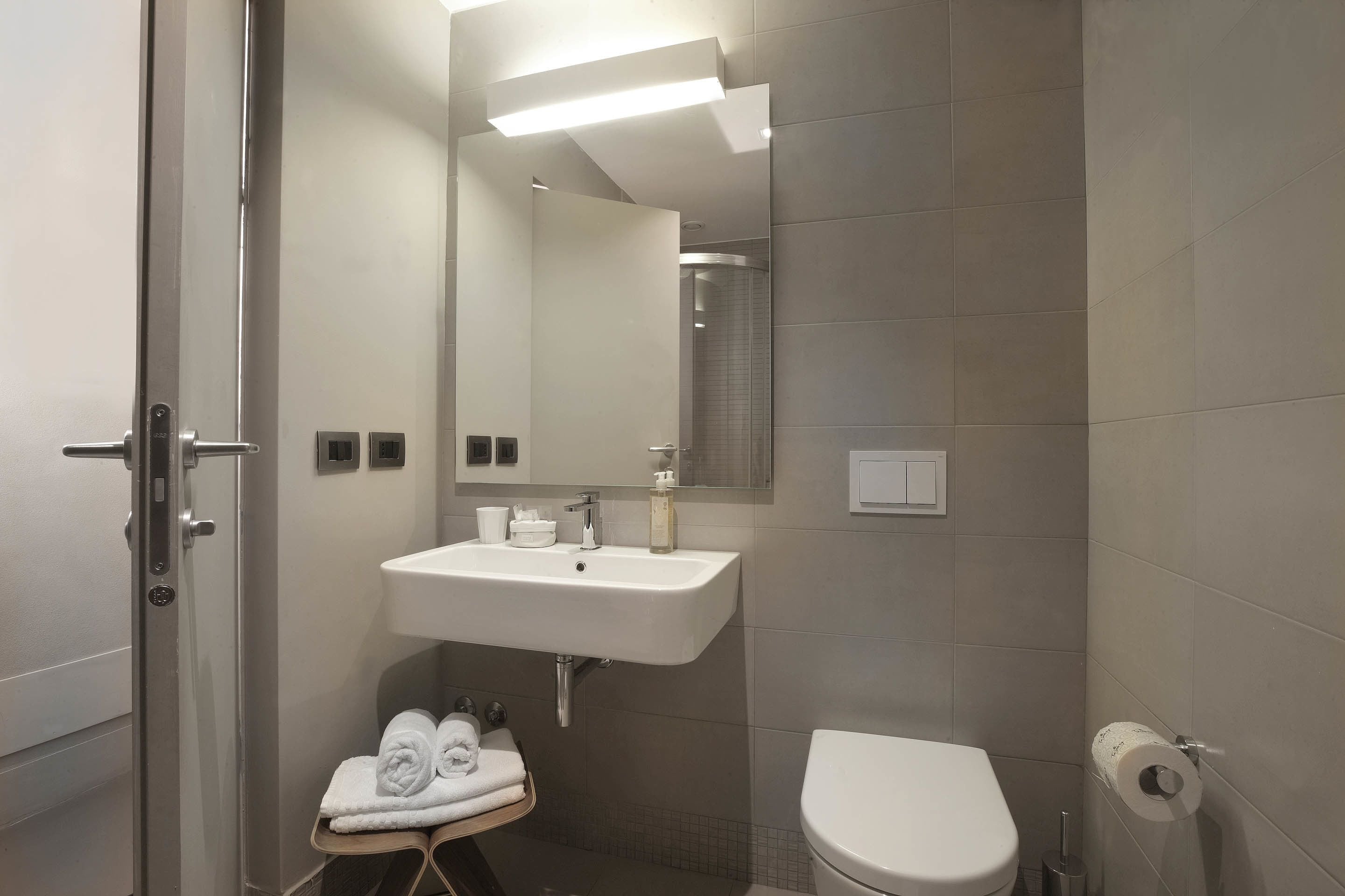 A modern bathroom with a white sink, a toilet, a towel rack with towels, and a mirror.