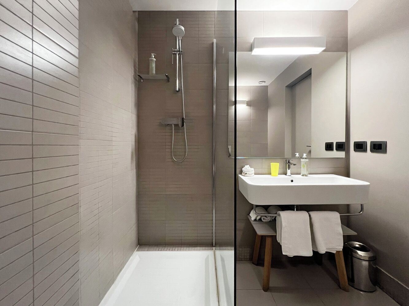 Un bagno moderno con cabina doccia in vetro, lavabo bianco e specchio.