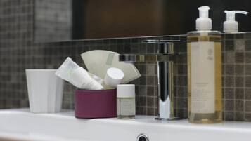 A bathroom counter with toiletries including a bottle of liquid soap, a container of cream, and a small bottle of lotion.