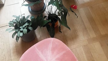 A round, pink ottoman on a wooden floor with several potted plants around it.