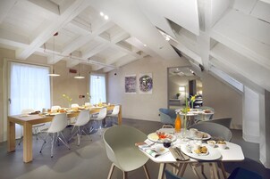 Zona pranzo moderna con soffitto alto, travi a vista e vista sulla stanza adiacente.