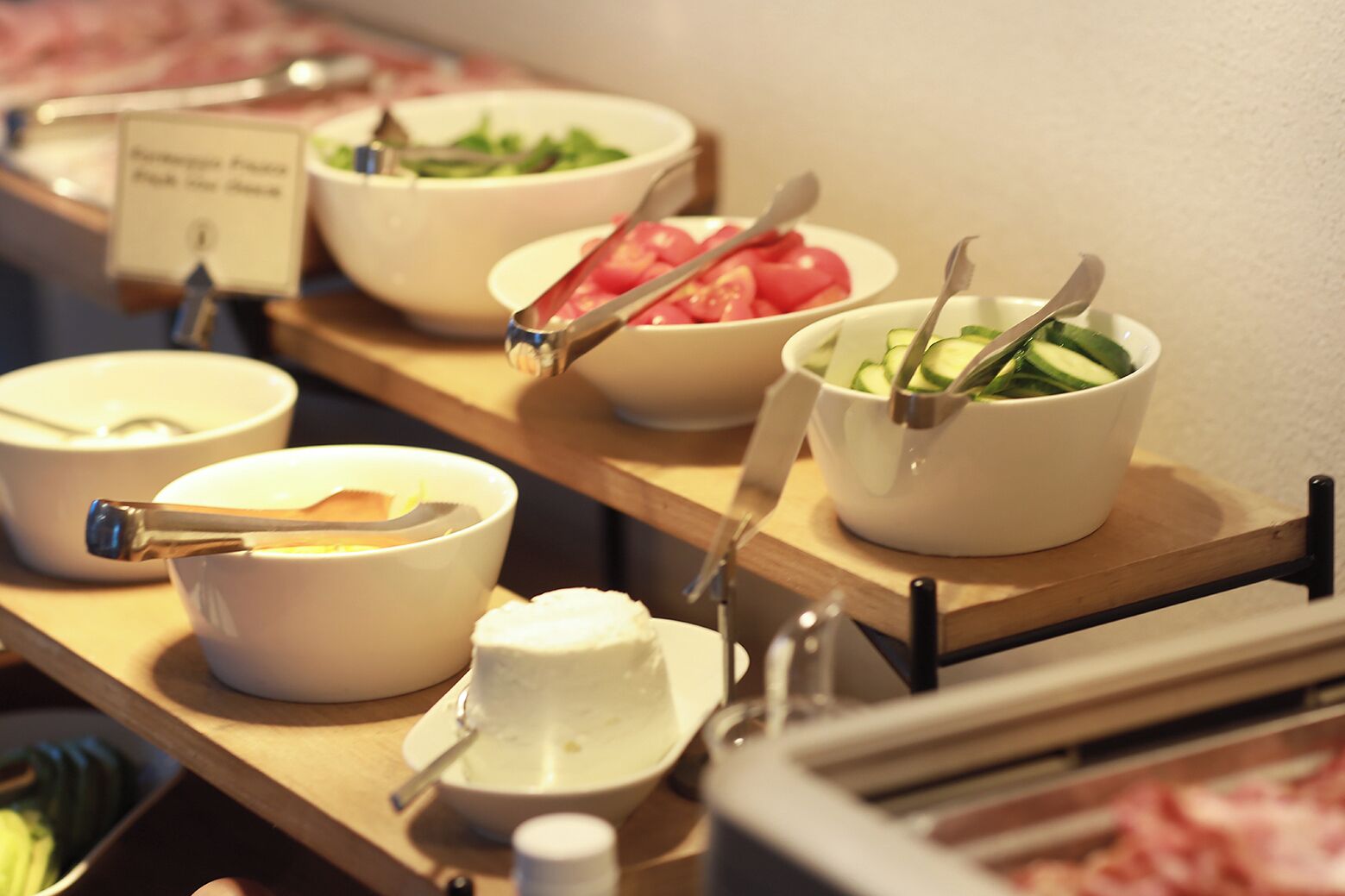 Ein Buffet mit verschiedenen Speisen, darunter eine Salatschüssel, eine Tomatenschüssel und eine Gurkenscheibenschüssel.