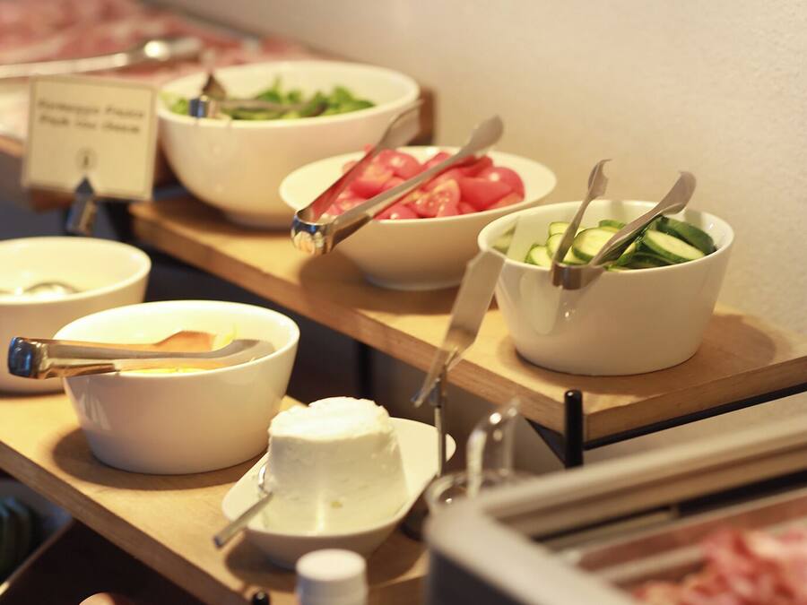 Ein Buffet mit verschiedenen Speisen, darunter eine Salatschüssel, eine Tomatenschüssel und eine Gurkenscheibenschüssel.