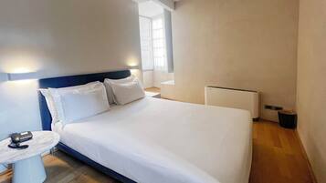 A modern hotel room with a large bed, bedside table with a lamp, and a small table with a phone.