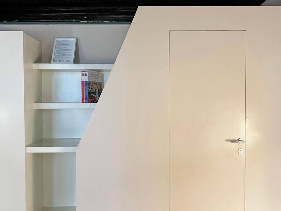 A room with a white wardrobe, a bookshelf with books, and a tiled floor.