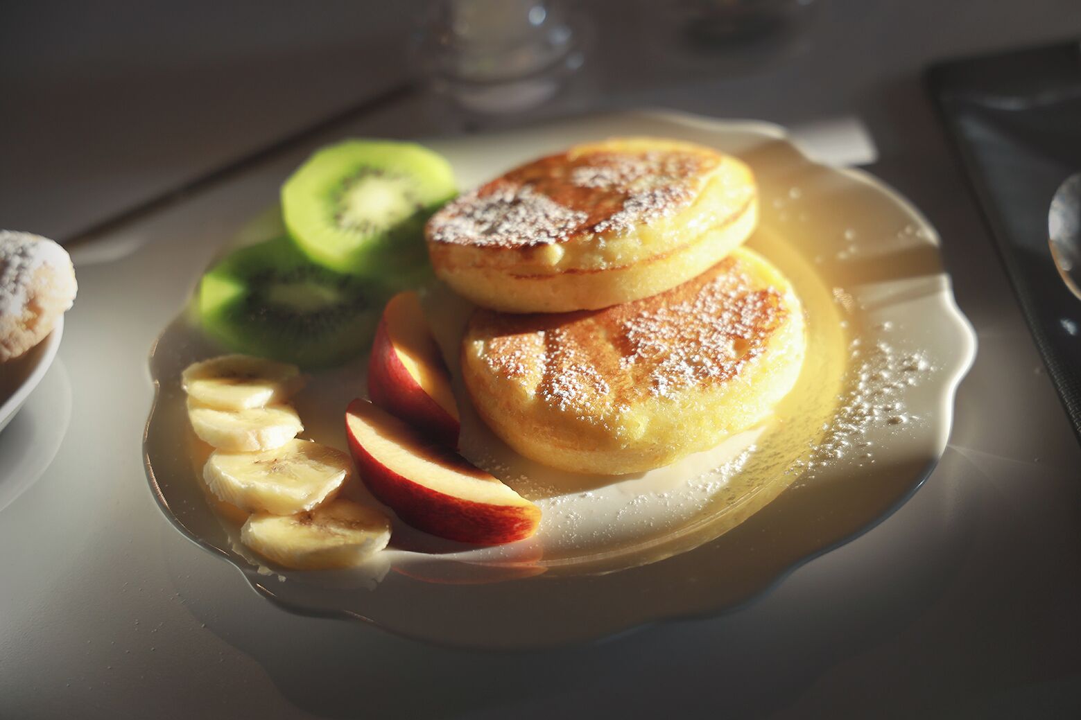 Un plato con tortitas, rodajas de manzana y kiwi sobre una mesa.
