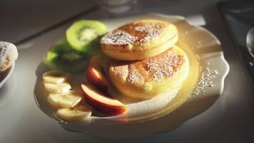 Een bord met pannenkoeken, plakjes appel en kiwi op een tafel.