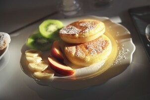 Een bord met pannenkoeken, plakjes appel en kiwi op een tafel.