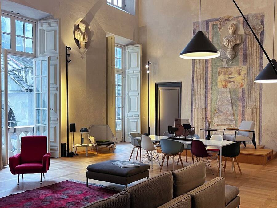 Een ruime woonkamer met een hoge nok, grote ramen en een eethoek met moderne meubels.