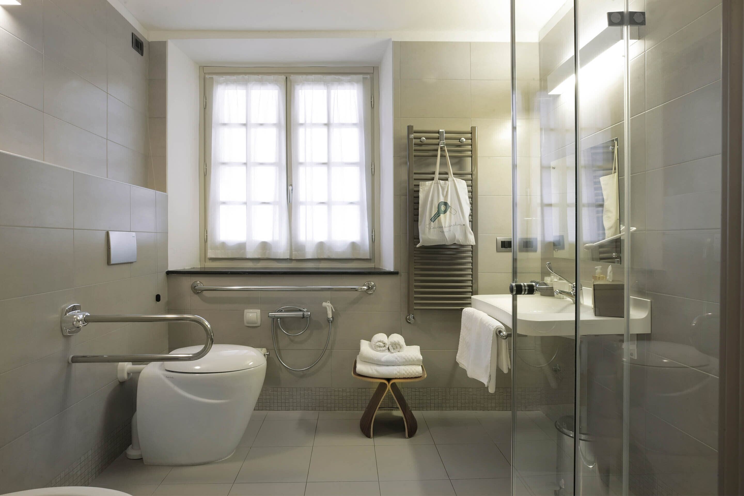 Une salle de bain moderne équipée de toilettes, d’un bidet, d’une douche à parois de verre et d’un petit tabouret sur lequel sont posées des serviettes.