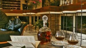 A spacious living room with a leather sofa, a coffee table with books and a flower, and a bookshelf in the background. - Hôtel des Roches (Les Eyzies)