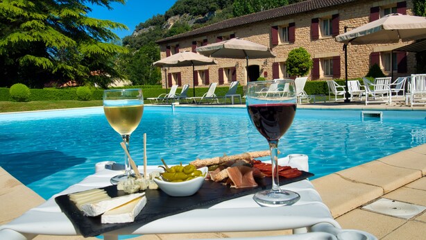 A poolside table with a cheese platter, two glasses of wine, and a view of a stone building with red shutters. - Hôtel des Roches (Les Eyzies)