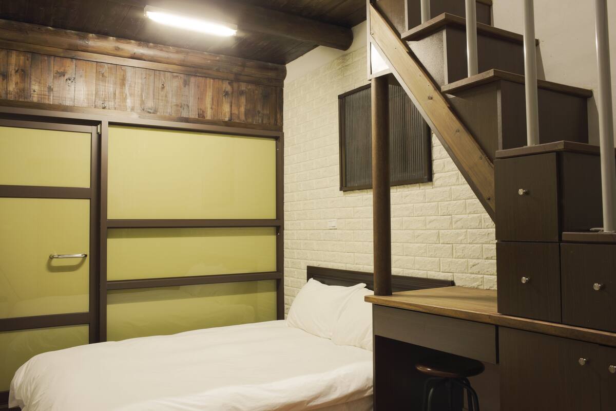 A bedroom with a bed, a wooden staircase, and a white brick wall.