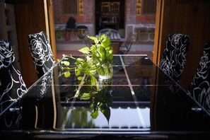 Taula de vidre amb una planta en test, envoltada de cadires amb tapisseria floral negra.