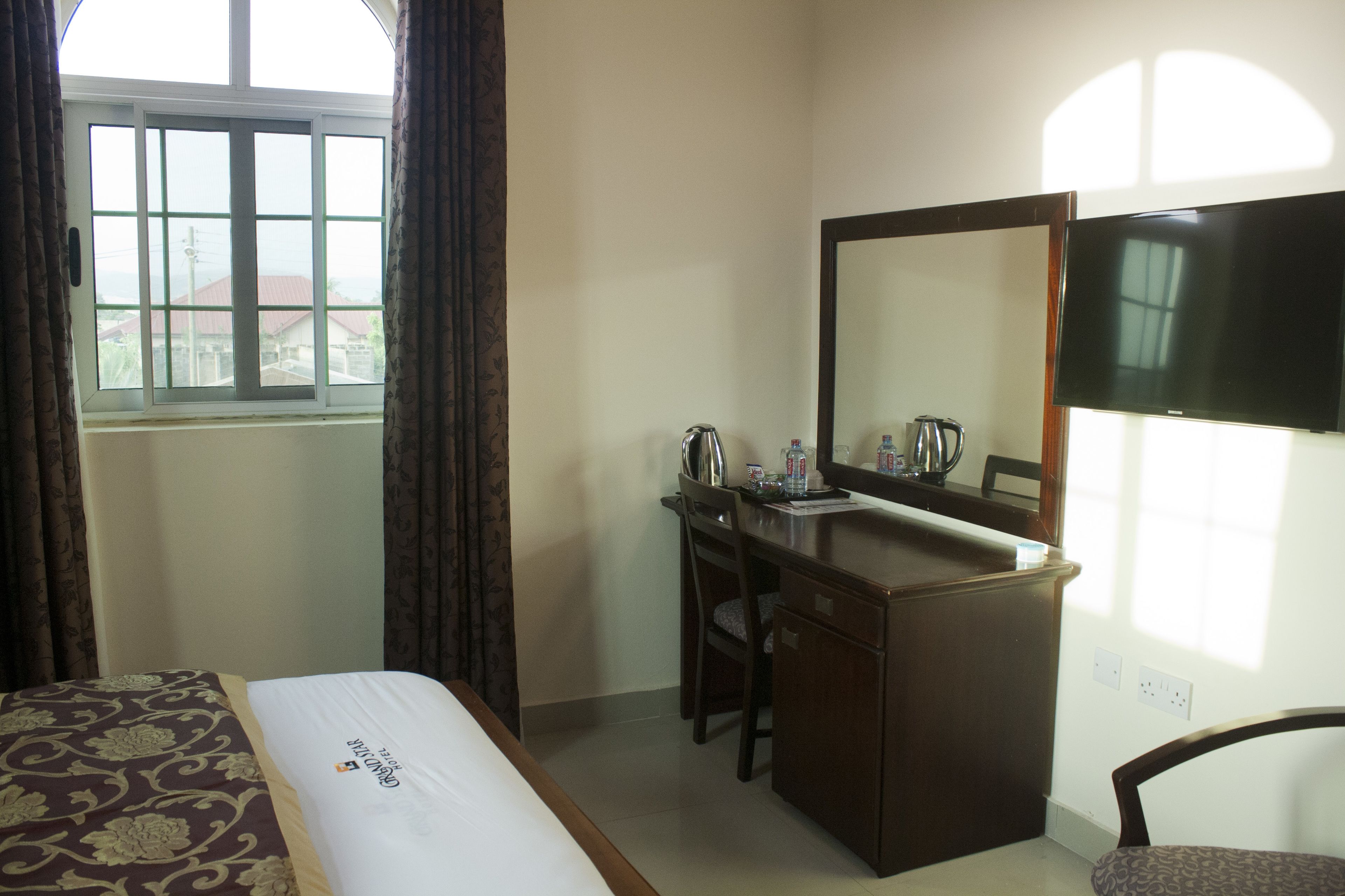 Una habitación de hotel con una cama, un escritorio, una silla, un espejo y un televisor.