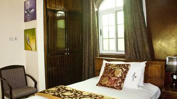A hotel room with a bed, a chair, a window with curtains, and artwork on the wall.