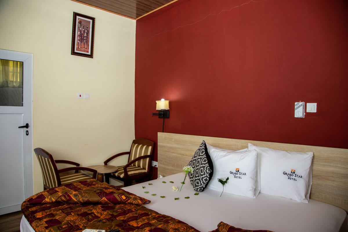 A hotel room with a bed, a chair, a small table, and a wall-mounted lamp.