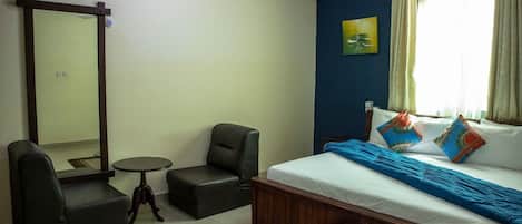 Quarto de hotel com cama, duas poltronas, uma mesa pequena, um espelho e um quadro na parede.