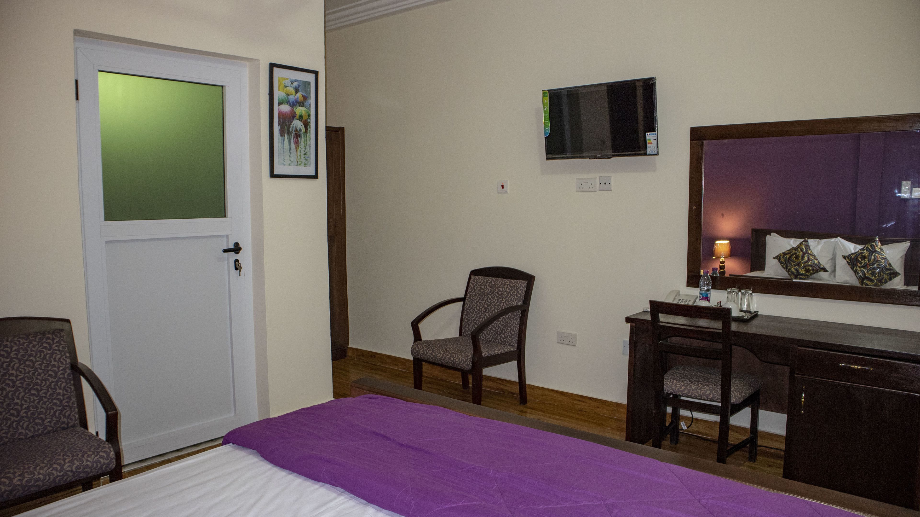 A hotel room with a bed, a desk, a chair, a television, and a door.