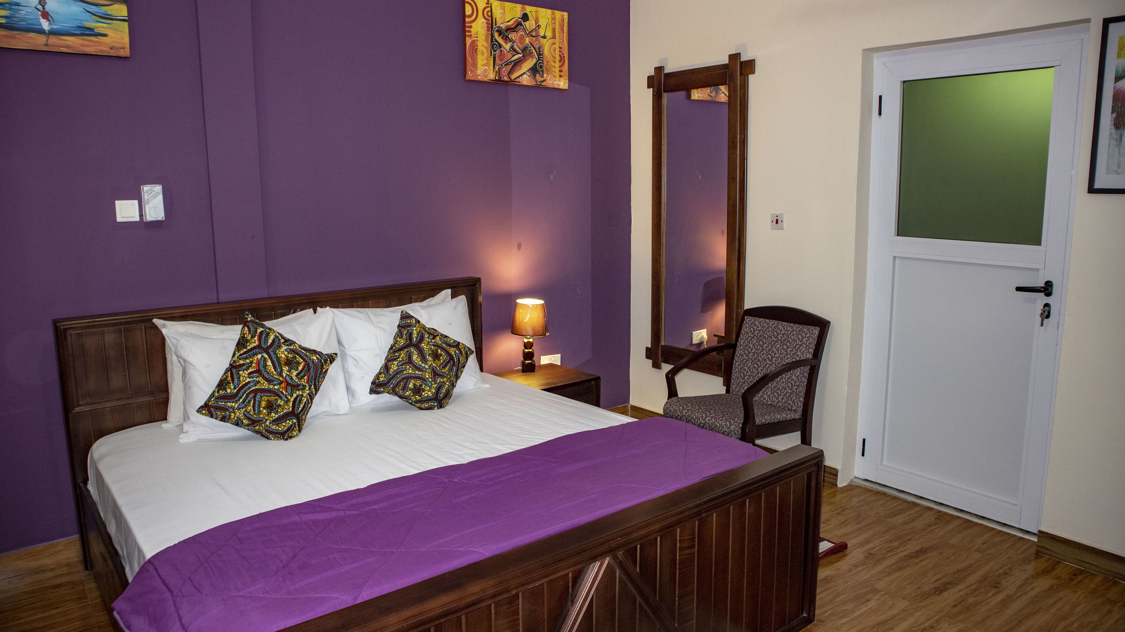 Une chambre à coucher avec un lit en bois, des murs violets, une chaise et une porte.