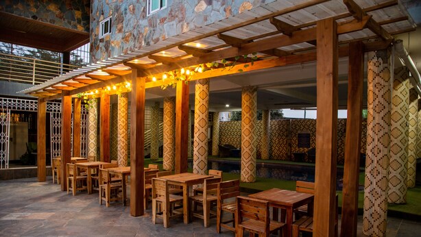 An outdoor patio area with wooden tables and chairs, stone flooring, and patterned columns. - Grand Star Hotel (Accra)