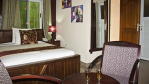 A hotel room with a bed, a chair, a table with two glasses of wine, and two paintings on the wall. - Grand Star Hotel (Accra)