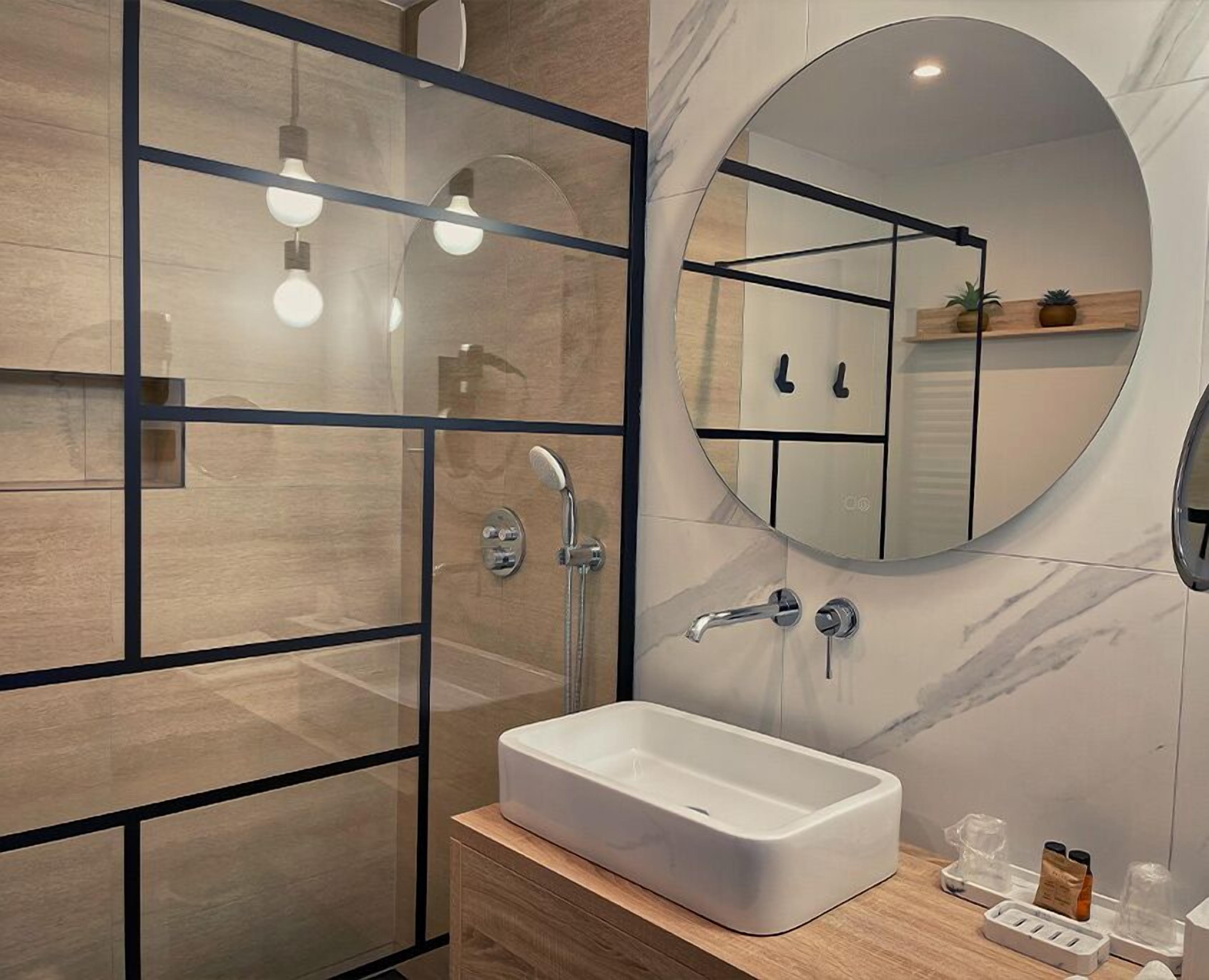 A modern bathroom with a glass shower enclosure, a white sink, and a large mirror.