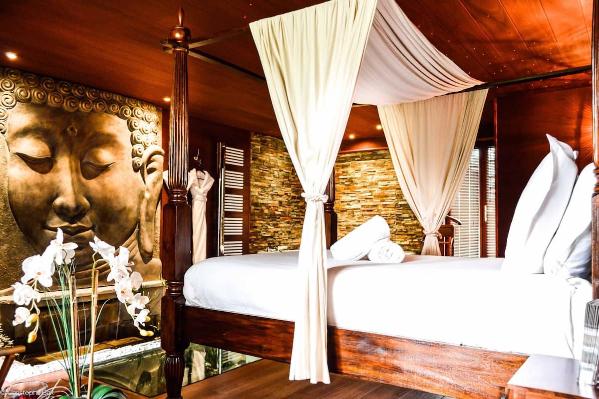 A bedroom with a large Buddha statue, a canopy bed, and a stone wall.