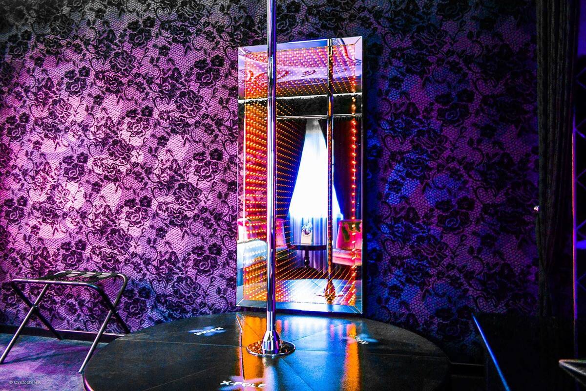 A room with a patterned wallpaper, a reflective surface, and a small stool.