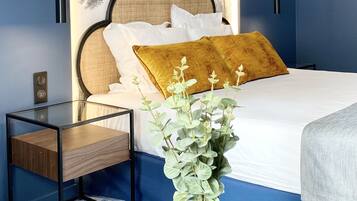 Quarto com cama, mesa de cabeceira, vaso com flores e parede com painel de árvore.