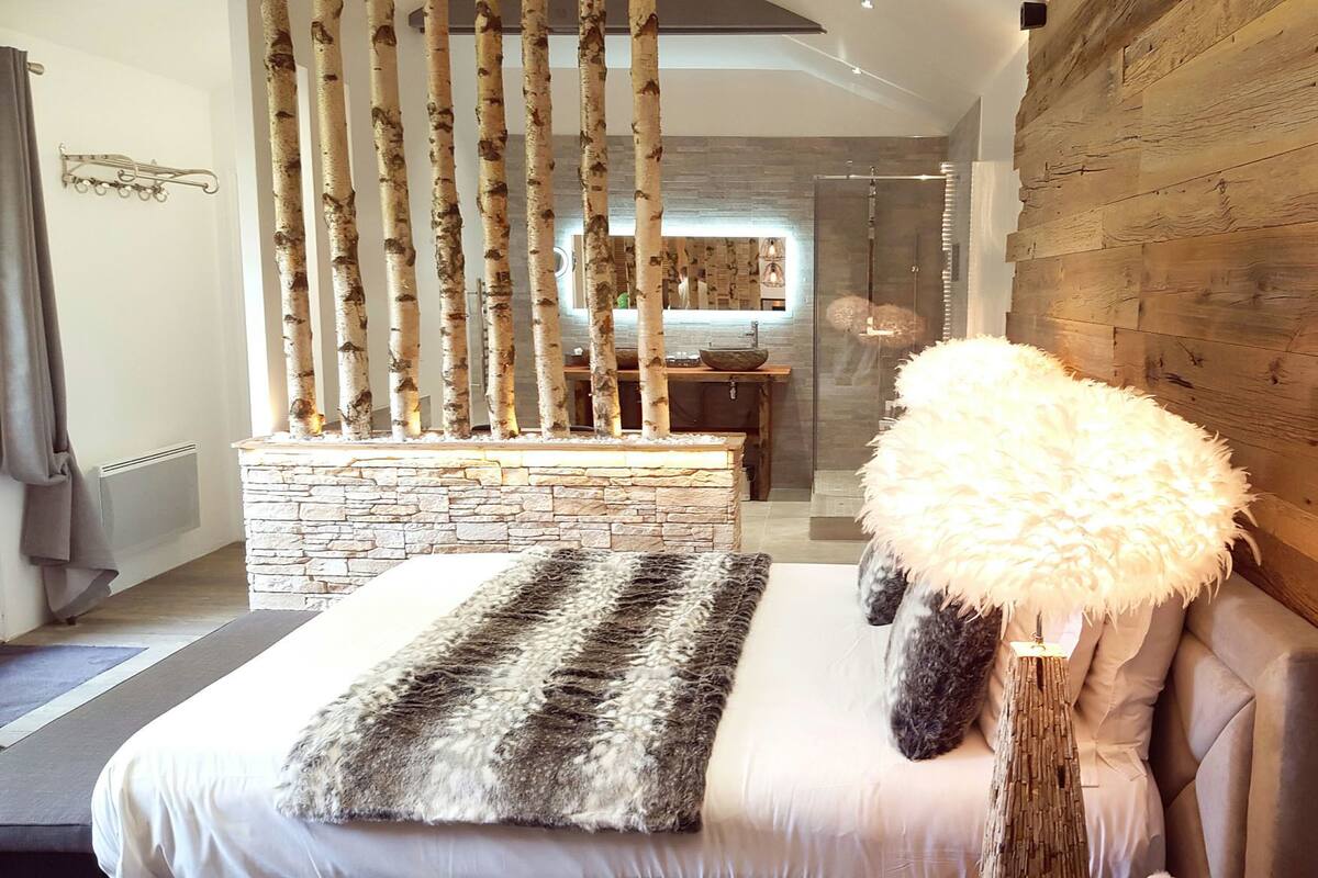 A modern bedroom with a stone fireplace, a fluffy white pouf, and a stone bench.