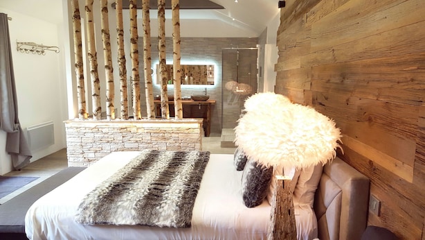 Un dormitorio moderno con chimenea de piedra, un otoman blanco mullido y un banco de piedra.