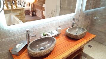 A bathroom with two stone sinks, a wooden vanity, a mirror, and a shower area.
