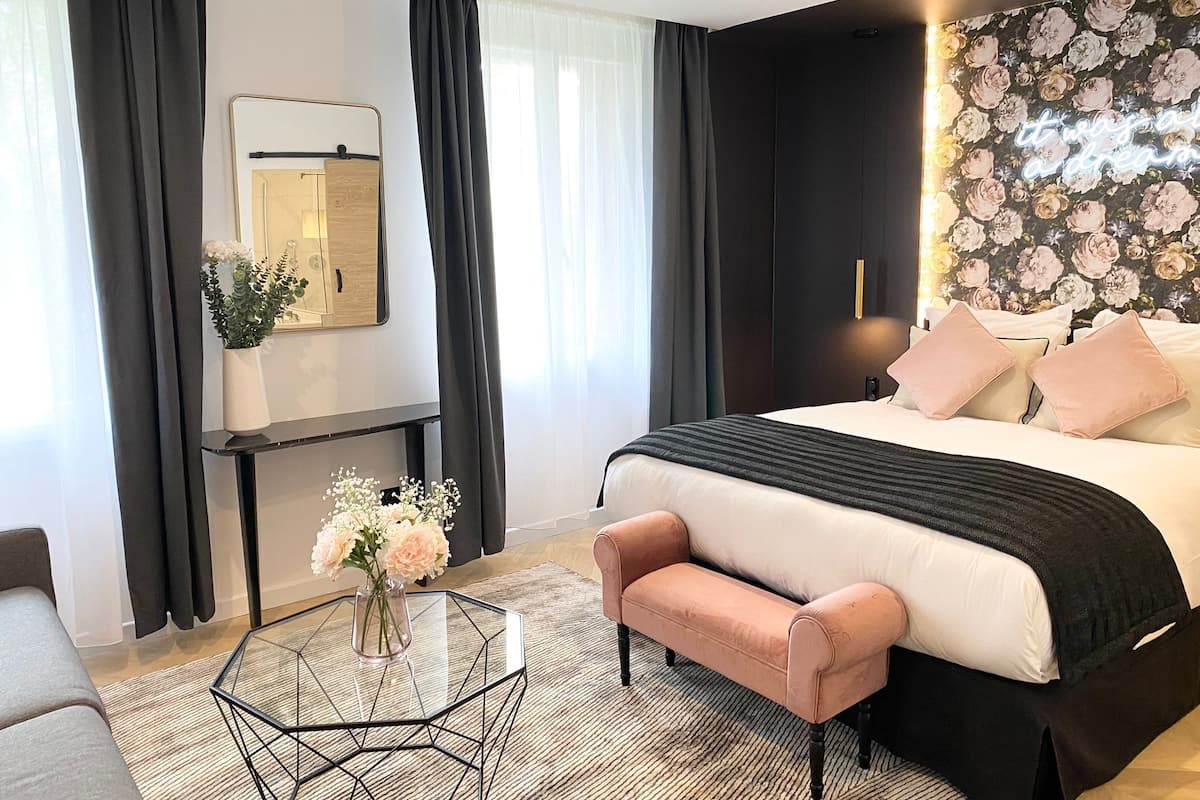 A modern hotel room with a large bed, a small sofa, a glass coffee table, and a mirror on the wall.