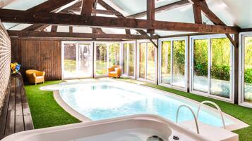 An indoor swimming pool with a hot tub, wooden beams, and large windows.