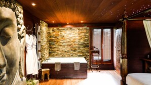 Un baño con pared de piedra, una bañera de madera y una estatua grande.