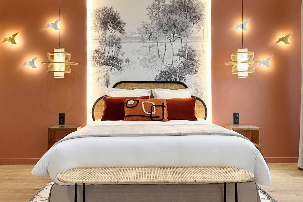 A bedroom with a large bed, two bedside tables, a wall-mounted artwork, and two wall-mounted lights.